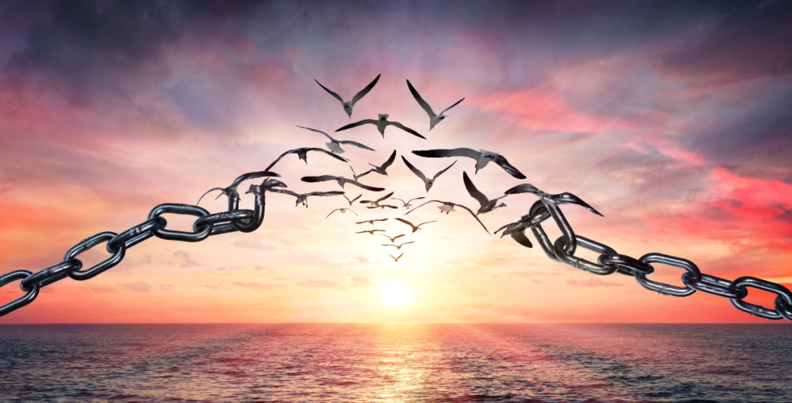 Broken chains transforming into birds flying toward a sunrise over the ocean